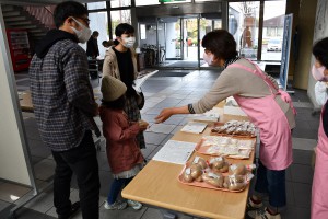 厚真町文化祭会場で推進員が来場者に厚真産食材とレシピを配布している写真
